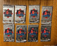 Front view of eight sealed silver foil 1992-93 McDonald’s All Stars hockey card packs arranged in two rows of four on a wooden surface.