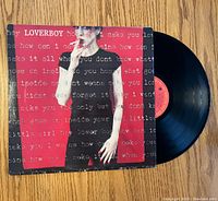 Front cover of Loverboy vinyl album with record partially visible on hardwood floor.