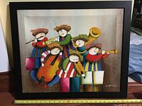 Frontal image of framed colorful cartoon-like figures playing musical instruments, showing the artwork and black frame with measuring tape revealing dimensions.