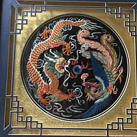 Close-up of needlepoint dragon and phoenix artwork showing detailed embroidery and colors.