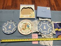 Three plates shown including two blue Jasperware Wedgwood plates and one colorful Peter Rabbit Christmas plate with original boxes