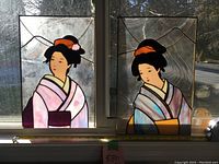 Two stained glass panels depicting Geisha women side by side in a window with daylight shining through.