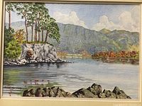 Close-up of the watercolor painting showing the signed artwork of a lakeside landscape with trees, rocks, mountains, and sky.