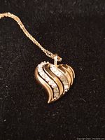 Close-up of the front side of the heart-shaped gold pendant with diamond inlays on a black background, showing the waved design and diamond details.