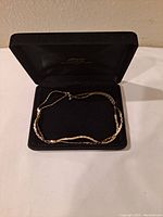 Gold tone necklace displayed in a black velvet case with a chain laid out showing its texture and length.