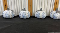 Four porcelain pumpkins decorated with blue and white sunflower pattern in a crackle finish, arranged side by side on a black surface.