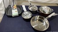 Full set of five cookware pieces on a table, including kitchen pots with lids and a cast iron grill pan.