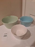 Set of three ceramic bowls in white, green, and blue placed on a flat surface, showing size differences and solid colors with no patterns visible.