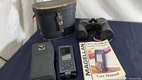 Photo showing Sears binoculars model 6282, black with amber coated lenses, their worn black leather carrying case, Magellan GPS ColorTrak device with color screen, soft protective case, and user manual.