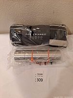 Photo showing the Slowtide fleece blanket rolled with label visible, accompanied by a sealed stainless steel thermos held by orange bands.