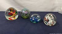 Front view of four glass paperweights showing swirled, spotted, bubble, and splatter patterns