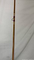 Full length view of the Heddon Pal 8355 Mark II fly fishing rod against a white wall, showing the natural finish wood shaft and detailed thread wraps.