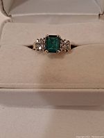 Front view of ring in presentation box showing emerald center and diamond accents
