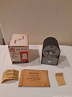 Full display of the coin meter with the original box and three instruction papers laid out in front.