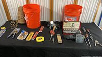 Photo of entire tool collection with 2 orange buckets, various hand tools and accessories spread out on black cloth.