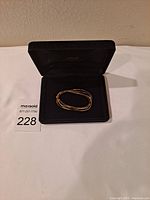 Napier gold tone thin necklace shown coiled in a black jewelry case placed on a flat surface.