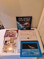 Photo of hardcover book 'The Space Telescope' by David G. Hitelman, spiral-bound booklets, and loose photos arranged on a bed.