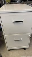 Front view of the white two-drawer metal filing cabinet showing the curved handles and cabinet surface.