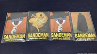 Four tin metal Sandeman Port and Sherry advertising signs displayed in original packaging, showing colorful vintage artwork and branding from Smalt.