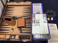 Photo showing open vintage Aries backgammon game set with plaid cloth and leather case, game pieces, dice, and adjacent Cardinal Mexican Train dominoes set in tin case with tiles and accessories.