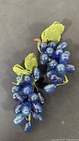 Photo showing two bunches of blue glass grapes with attached green leaves and stems on a dark surface.