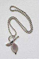 Full view of the sterling silver ball bead necklace with leaf pendant and toggle closure on a white fabric background.