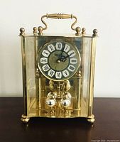 Front view of brass carriage clock with visible clock face and pendulum balls inside glass case