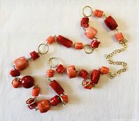 Close-up of various coral beads including round, cylindrical, and square shapes with gold plated links on white cloth background.