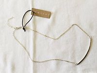 Full view of sterling silver chain necklace laid on white cloth background showing chain links, curved bar accent, and attached hang tag.