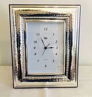 Front view showing hammered sterling silver rectangular frame and clock face with black numerals and hands, stamped 'Ag 7g'