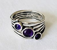 Close-up of sterling silver artisan ring showing three purple stones and band detail.