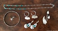 Photo of the sterling silver turquoise bead necklace, silver bangle bracelet, two pairs of earrings including coin hoop and dangle turquoise shell design, and two leaf motif pins/brooches on wooden surface.