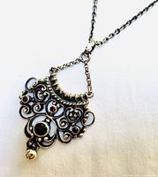 Close-up of vintage sterling silver pendant showing intricate scrollwork and red garnet stones.