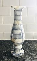 Full front view of tall blue onyx mosaic vase sitting on a dark countertop with a white tile backsplash