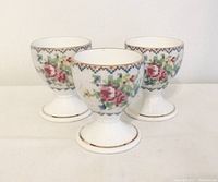 Three Royal Albert Petit Point egg cups showing front petit point floral pattern and gold trim.
