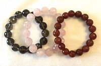Three stretch faceted quartz bead bracelets in carnelian, pink quartz, and smoky topaz colors shown side by side on white background.
