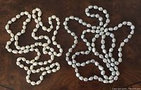 Two pearl necklaces coiled loosely on a wood surface. Cream and grey colored pearls are visible, shape is irregular oval, no clasps visible.