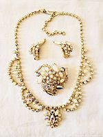 Full view of vintage rhinestone parure set including necklace, brooch, and earrings laid out on white background.