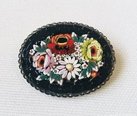 Front view of oval vintage micro mosaic brooch with multi-coloured floral designs in black frame