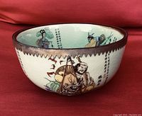 Side view of the celadon bowl showing hand-painted figures of the eight immortals, Chinese calligraphy, and metal overlay rim with jagged edge and dragon decoration.