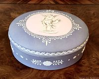 Top and side view demonstrating matte blue finish with raised white floral motifs and pink oval medallion with cherub angel.