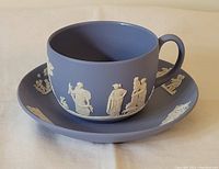 Side angle of blue Jasperware teacup sitting in matching saucer showing detailed white relief decoration.