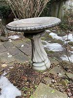 Full view of the bird bath showing the separate circular top resting on the fluted columnar base outdoors with some snow around the area.