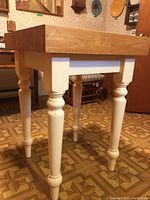 Side view showing thick butcher block top with natural wood finish and cream painted turned legs bolted to the table top.