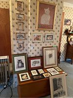 Wide view showing many framed cat prints arranged on wall and on furniture, varying sizes and frame styles.