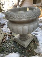 Concrete round planter with scalloped detailing on rim and bulbous texture below, shown outdoors on ground with some snow and dried foliage.