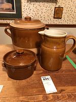 Photo of two brown stoneware crocks and one brown ceramic jug on wooden surface, showing size and overall condition