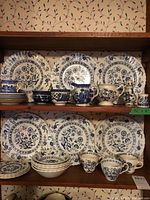 Wide view of shelf holding multiple blue and off-white Classic de G. Meakin Blue Nordic china pieces including plates, cups, creamer, sugar bowl, and bowls.