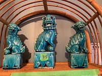 Front view of three blue ceramic foo dog figurines on a rattan shelf, largest marked 7.5 inches tall.