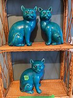 Front view of two larger turquoise blue ceramic cat figurines seated on wicker shelf, showing details and size.